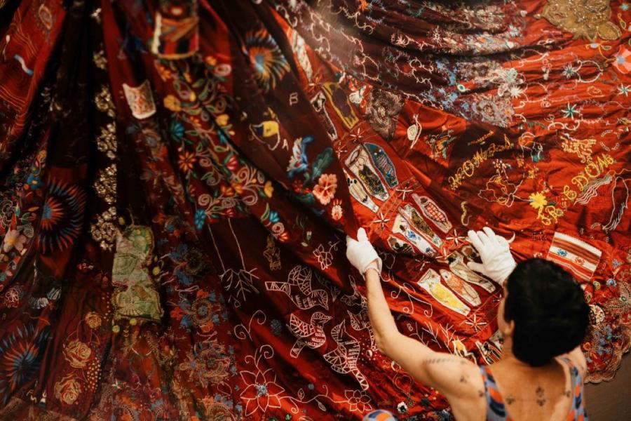 A close up of the bottom of the red dress being arranged by a person in white gloves